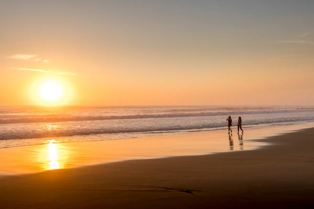 Deux promeneurs marchant au bord de l'eau sur une plage, au soleil couchant